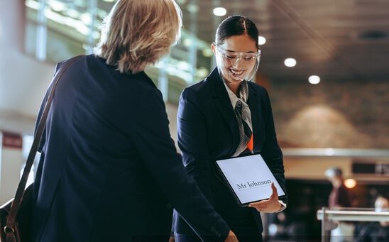A chauffeur holding a welcome sign at the airport arrival area while greeting an arriving businessman